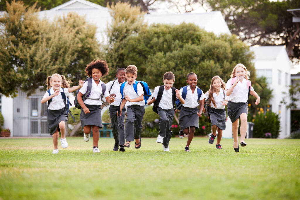 Excited Elementary School Pupils Wearing Uniform Running Across Field at Break Time